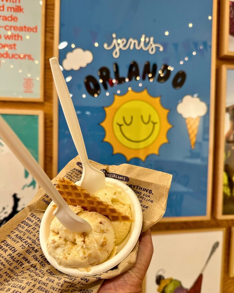Image of a cup of ice cream with two spoons in front of a Jeni's Orlando poster