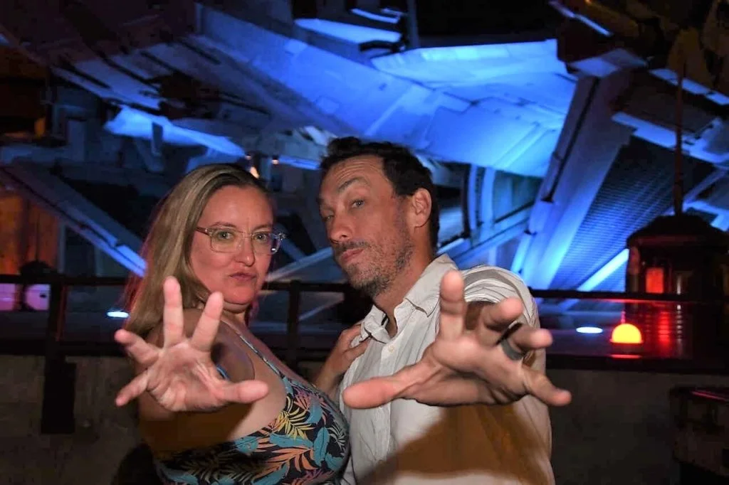 Star Wars Galaxy's Edge PhotoPass - Kylo Ren's Ship is lit deep blue in the background. Dani and husband Tim stand near the camera with their arms outstretched like they are using the Force.