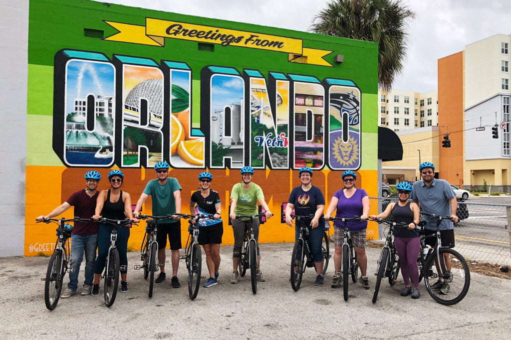 Bike Cubed tour group in front of Greetings from Orlando mural