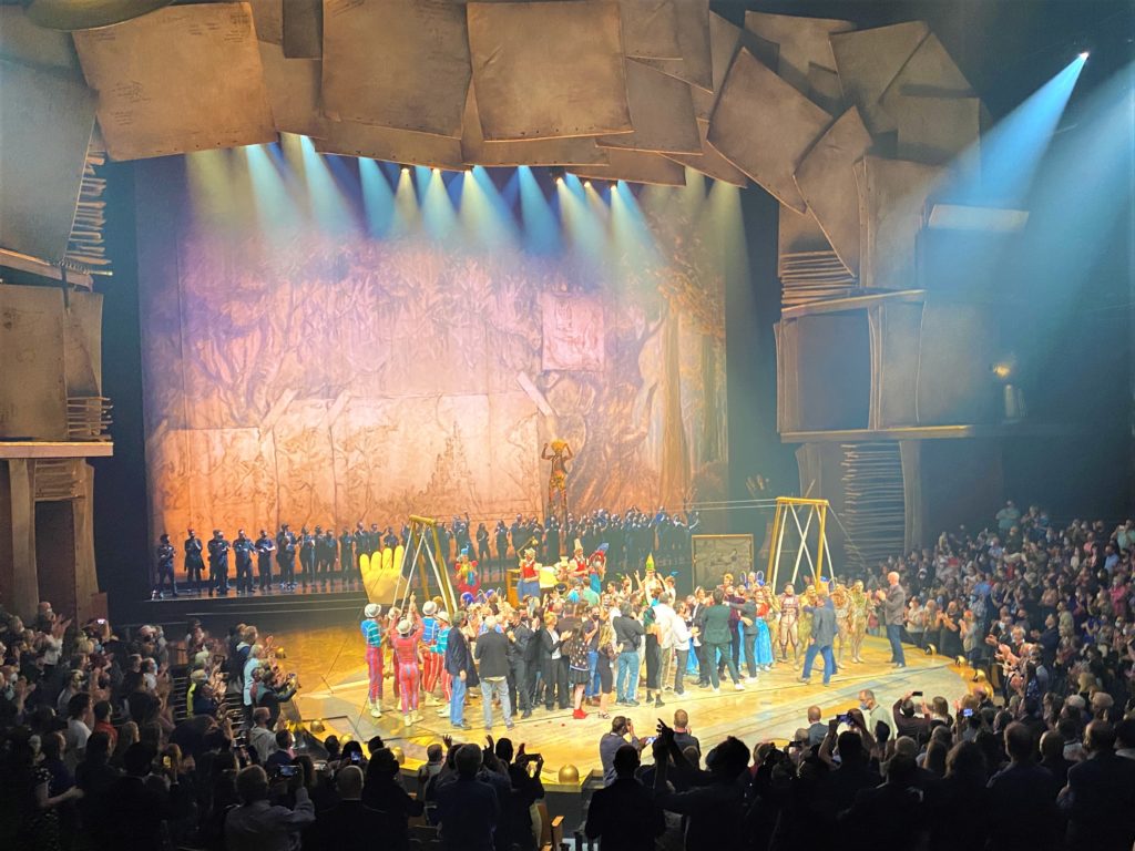 Cirque du Soleil Disney Springs - Drawn to Life Grand Opening Cast celebrate on stage after the performance. The stage is brightly lit and the audience is giving them a standing ovation.