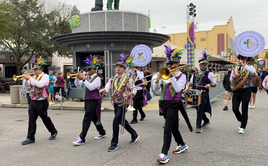 Universal Mardi Gras 2022 Parade Band marches through the New York area playing brass instruments and drums