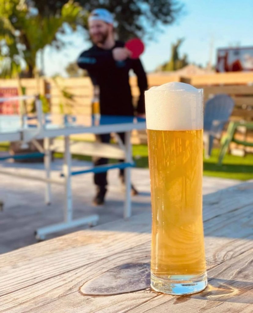 Gatlin Hall Brewing - one of Orlando's kid friendly breweries - this photo shows a light colored beer in a tall glass in the foreground and a man playing ping pong in the blurred background