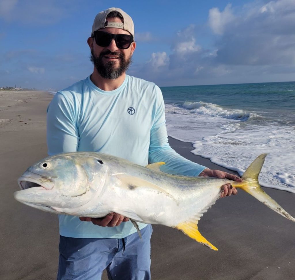 A man holds a large white and yellow fish caught during Cocoa Beach Surf Fishing while standing on the beach