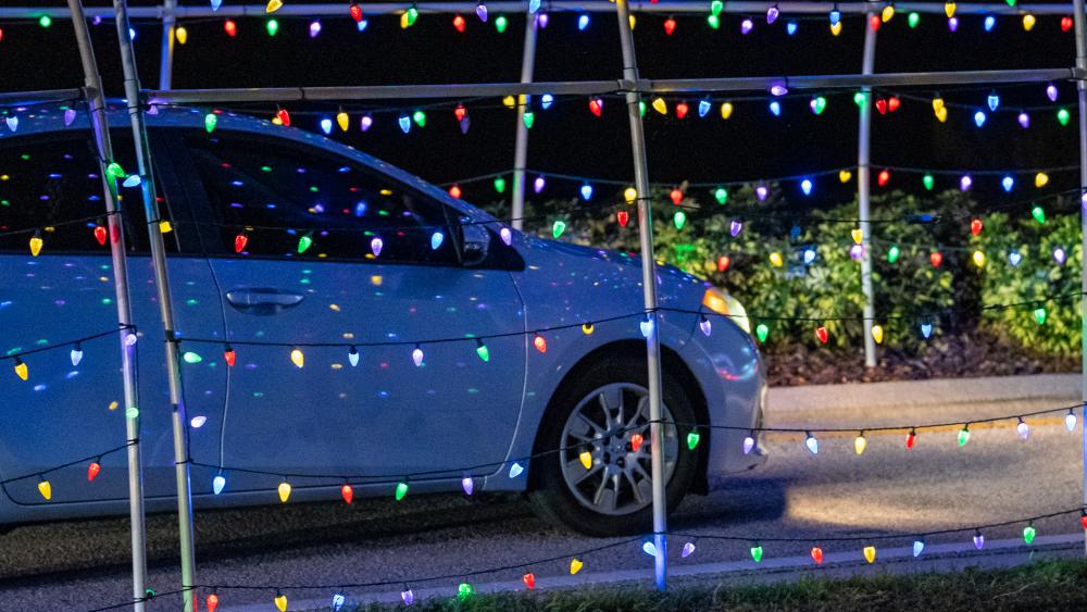 a white car drives through archways of christmas lights