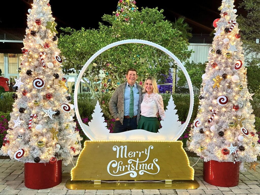 Image of a man in woman in a snow globe photo op between two Christmas trees at Holiday Lights at Ocala's World Equestrian Center Winter Wonderland