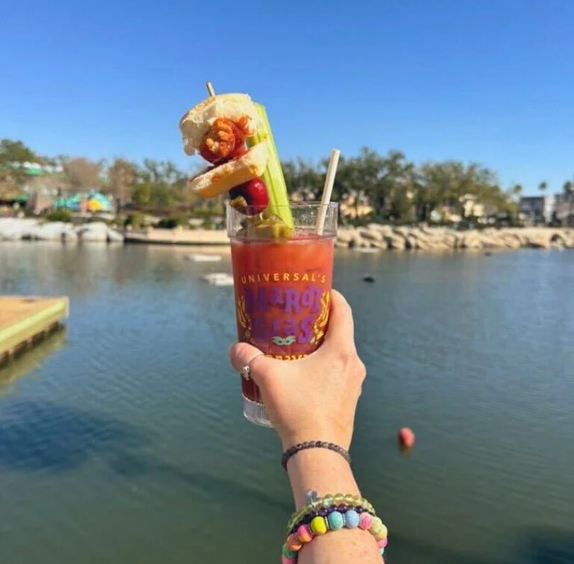 holding a bloody mary cocktail with a variety of toppings including a mini chicken slider