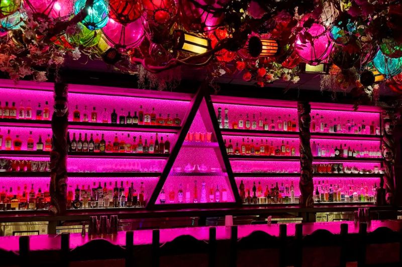 tiki bar backlit by hot pink lights, rum bottles on shelf, nautical tiki lights overhead